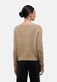 Pull en laine beige à coupe décontractée, avec un col côtelé et des manches longues. Présente une longueur cropped et une finition douce et texturée.