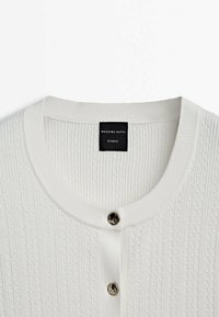 Cardigan blanc tricoté avec texture côtelée, encolure ronde et deux boutons argentés brillants à l'avant, étiquette Massimo Dutti Studio à l'intérieur.