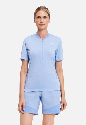 Woman wearing light blue short-sleeve zip-up top and matching shorts, standing against plain white background.