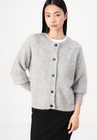 Cardigan en laine gris avec un col rond, texture côtelée et six boutons noirs sur le devant. Présente des manches trois-quarts et une longueur cropped.