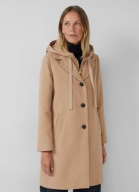 Manteau beige avec capuche, design croisé, grands boutons et poches latérales. Le tissu a une texture lisse avec un léger éclat.