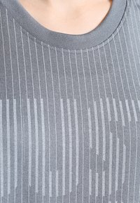 Grijze gebreide top met een ribbelstructuur en verticale strepen in een gradientpatroon. De halslijn heeft een gladde, ronde kraag.