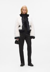 Faux fur jacket in black and white, featuring a cropped design, wide sleeves, and contrasting textures. Paired with tailored black trousers.