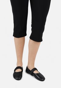 Bailarinas de cuero negro con puntera redonda, que cuentan con una tira elástica recogida a lo largo del mediopié. Combinadas con leggings negros cortos.