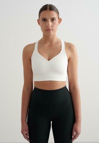 Biely rebrovaný crop top s výstrihom do V a širokými ramienkami. Skombinovaný s čiernymi rebrovanými legínami s vysokým pásom. Hladká textúra, priliehavý dizajn.
