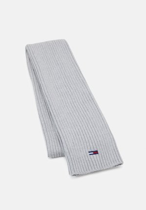 Jasnoszary szalik z prążkowanego dzianiny, złożony, z małym prostokątnym logo w paski niebieskie, białe i czerwone, umieszczonym w pobliżu jednego końca.