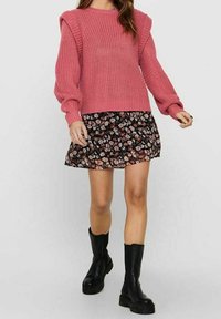 Różowy sweter o fakturze z bufiastymi rękawami, w połączeniu z czarną mini spódnicą w kwiaty. Modelka nosi czarne masywne botki.