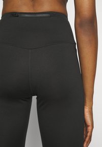 Leggings neri a vita alta realizzati in un tessuto liscio ed elastico, dotati di una tasca con zip nascosta sul retro e dettagli con cuciture piatte.