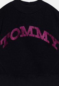 Črna srajca s kapuco, ki ima izbočeno, sijočo roza "TOMMY" napisano čez prsi. Teksturni material z rebrastim ovratnikom in robom.