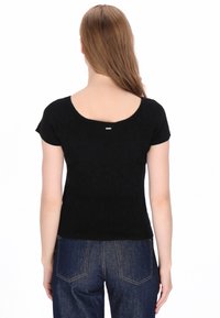 Fekete bordázott rövidujjú felső, amely mély kivágású hátoldallal és egy kis ezüst díszítéssel rendelkezik a nyakkivágás közelében. Sötét farmernadrággal viselve.