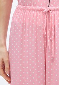 Ροζ ύφασμα με λευκές πουά, με ελαστική μέση και ρυθμιζόμενο κορδόνι δεμένο στη λεπτομέρεια. Λεπτή υφή, ελαφρύ σχέδιο.