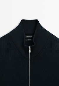 Mörkblå bomullszip-sweater med ribbat mönster och hög krage. Silverfärgad dragkedja ger en elegant detalj.