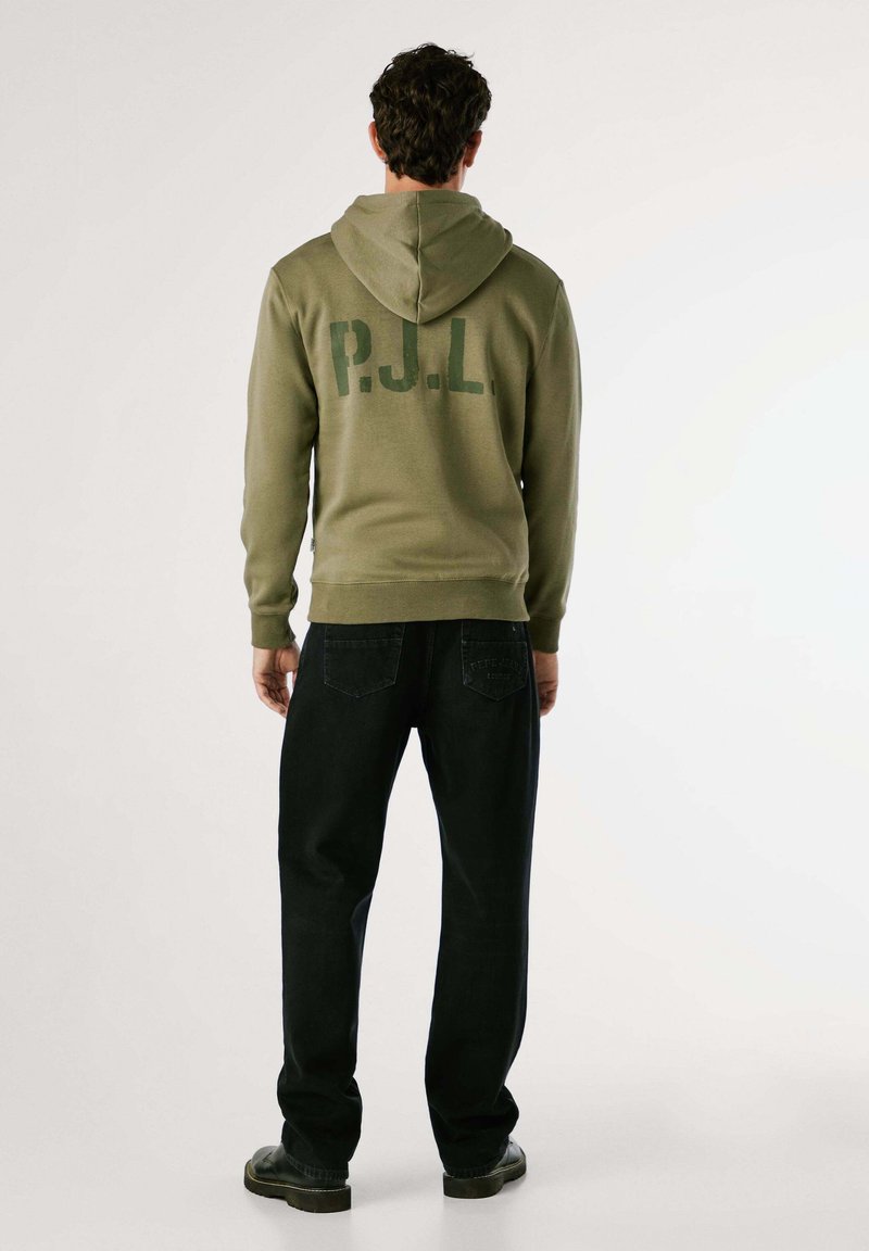Groene hoodie met grote "P.J.L." opdruk op de achterkant, gecombineerd met zwarte jeans en zwarte schoenen, met een recht model.