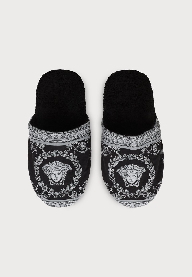 Black slip-on slippers with soft lining and white intricate Medusa head and laurel wreath pattern on the top.