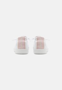 Sneaker bianche a bassa scarpa viste dal tallone, caratterizzate da un tessuto testurizzato con strisce verticali pesca e beige sulla parte posteriore.