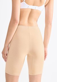 Beige vysoké tvarující šortky vyrobené z elastického materiálu, s hladkou texturou a přiléhavým střihem, dosahujícími k polovině stehna.