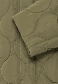 Giacca di tessuto verde oliva trapuntata con motivo di cucitura arrotondato; texture liscia; presenta una manica piegata con dettaglio al polsino.