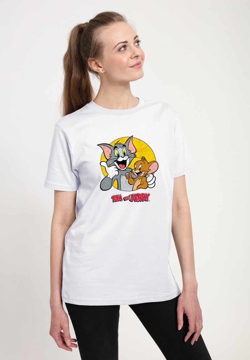 Hvid bomulds T-shirt med et farverigt grafisk motiv af Tom og Jerry på en gul cirkel baggrund. T-shirten har korte ærmer og rund hals. 