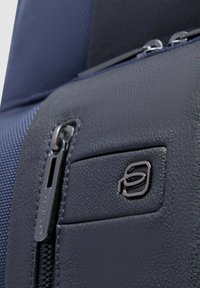 Zaino blu navy con materiale testurizzato simile alla pelle con finitura liscia, tasca con cerniera e dettaglio logo metallico.