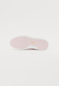Pink rubber sole with textured surface and white edge, featuring circular patterns and gold brand logo. Flat shape designed for grip.