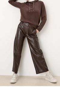 Brun hoodie med snören som är matchad med hög midja bruna faux läder vida byxor, accentuerad med framfickor och beige sneakers.