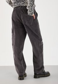Gray corduroy trousers with a relaxed fit, elastic waistband, and side pockets. Worn with black boots, showcasing texture and design.