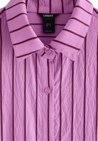 Lyse lilla skjorte med mørk lilla lodrette striber, krave og knaplukning foran. Stoffet ser krøllet ud.