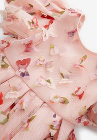 Rosa nätklänning med lager av blommiga applikationer i olika färger, med en strukturerad design och en rund halsringning.