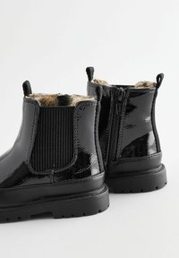 Stivaletti in vernice nera con cerniera laterale, pannello elastico, suola in gomma spessa e fodera in pelliccia sintetica leopardata.