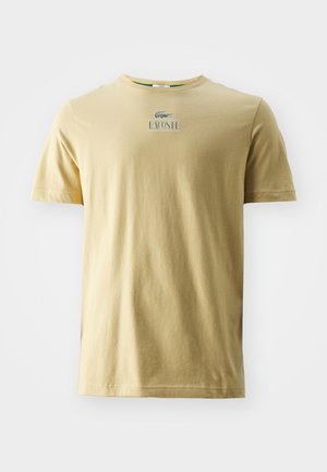 Tričko s krátkym rukávom a okrúhlym výstrihom vo svetložltej farbe z bavlny, s logom Lacoste v zelenej a bielej farbe na hrudi.