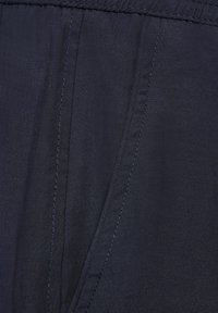 Mörk marinblått tyg som visar en slät textur, med subtila sömnadsdetaljer och en plan midjebandsdesign.