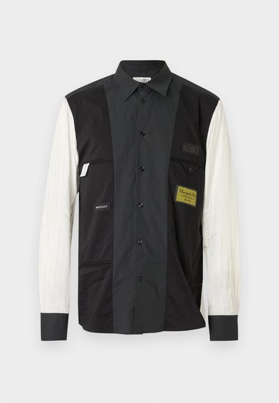 Košile na knoflíky s černými a bílými částmi, obsahující kapsu na černé straně, texturované bílé pruhy na rukávu a značkové nášivky.