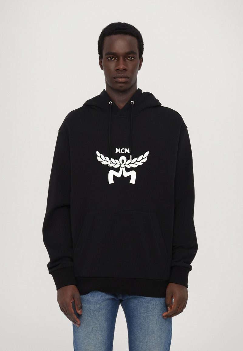 Sweat à capuche noir avec cordon de serrage, arborant un logo blanc et un motif de feuille sur la poitrine. Poche avant et poignets côtelés au niveau des manches.
