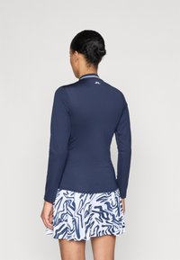 Top lungo navy con texture a coste e colletto a righe bianche, abbinato a una gonna bianca svasata con un motivo astratto navy.