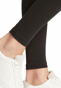 Zwarte leggings met een gladde, geribbelde textuur en een aangesloten ontwerp, gecombineerd met witte sneakers met een gestructureerde teentop en veters.