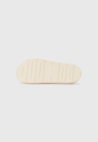 Rubber shoe sole, beige color, textured with horizontal grooves and ridges for traction, featuring a logo in the center.