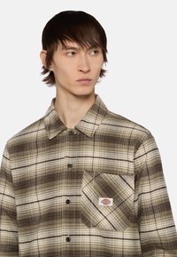 Bruin en beige geruite blouse met een kraag, knopen, borstzak aan de linkerkant en een label. Gemaakt van een gestructureerde stof.