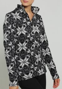 Schwarz-weiß gemusterter Pullover mit hohem Kragen, der geometrische Schneeflocken-Designs und einen Viertel-Reißverschluss aufweist. Weiche Textur.