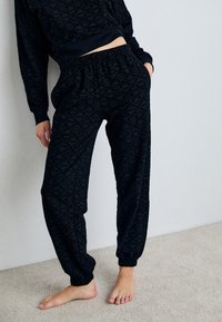 Felpa nera con motivo e pantaloni abbinati con vita e polsini elasticizzati, realizzati in un tessuto morbido. I motivi sono sottili e tonali.