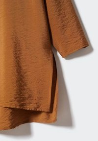 Bruine gemêleerde top met een subtiele glans, voorzien van een losse pasvorm, driekwartmouwen en een gebogen zoom voor een ontspannen silhouet.