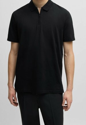 Czarna koszulka polo z krótkim rękawem, wykonana z miękkiego materiału, z połowicznym zamkiem błyskawicznym, klasycznym kołnierzykiem oraz prostym dołem z bocznymi rozcięciami.