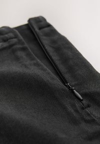 Schwarzer Stoff mit glatter Textur, der eine Nahaufnahme einer Reißverschlusstasche und ein dezentes Fischgrätmuster zeigt.