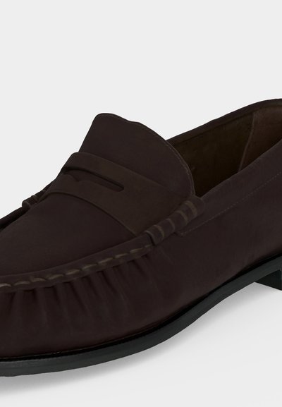 Mocassin homme en daim brun foncé, sans lacets, avec couture mocassin et semelle noire, vu de côté.