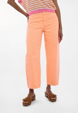 Jeans naranja brillante de pierna ancha con una textura suave. Combinados con sandalias de plataforma marrones que incluyen una hebilla decorativa y detalles de tachuelas.