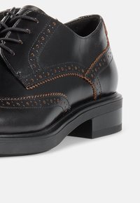 Svarte skinnsnøresko med brogue-design, perforerte detaljer og kontrasterende brune sømmer, samt block heel.