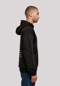 Black hooded sweatshirt with a front kangaroo pocket, ribbed cuffs, and colorful text graphic design on the back. Crafted from soft, textured fabric.