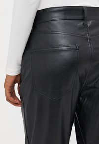 Calças de couro pretas com um design justo, bolsos traseiros visíveis e detalhes de costura subtil. Textura suave com um acabamento brilhante.