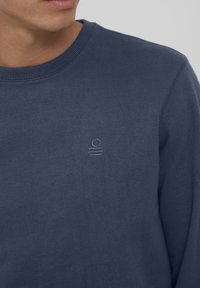 Felpa blu navy con scollo rotondo, caratterizzata da un piccolo logo ricamato sul petto. Realizzata in un tessuto morbido con una superficie liscia.