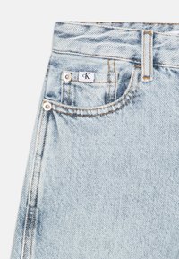 Světle modré džíny z denimu s viditelným prošíváním, stříbrnými komponenty a přední kapsou s bílou etiketou CK. Hladký povrch a standardní střih.