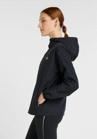 Svart huva jacka i lätt material, med fram zip och sidofickor, elastiska muddar och minimal logotyp.